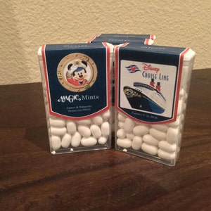 May include: Two small clear plastic containers filled with white mints. The containers have colorful labels with a Mickey Mouse character and a Disney Cruise Line ship. The labels also include the text "MAGIC Mints" and "Disney Cruise Line".