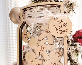Puede incluir: Adorno navideño de madera con forma de tarro de cristal con una etiqueta que dice "The Karas Family". Dentro del tarro hay cinco figuras de pan de jengibre de madera con los nombres "Ollie", "Colton", "Dad", "Jackson" y "Mom" escritos en ellas.