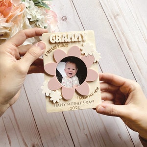 May include: A wooden photo frame with a flower design. The frame has the word "Grammy" at the top and the text "If you were a flower, I would pick you! Happy Mother's Day! 2024". The frame holds a photo of a baby.