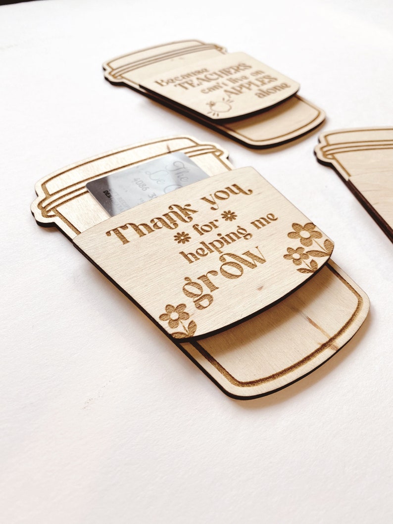 Puede incluir: Etiqueta de regalo de madera en forma de taza de caf&eacute; con el texto "Gracias por ayudarme a crecer" y un peque&ntilde;o dise&ntilde;o floral. La etiqueta est&aacute; dise&ntilde;ada para contener una tarjeta de regalo o una peque&ntilde;a nota.