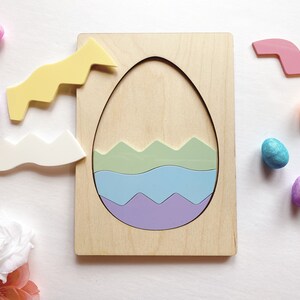 May include: A wooden puzzle board featuring a large egg-shaped cutout. Inside the cutout are three wavy-edged pieces in light green, light blue, and purple. Two additional wavy pieces in yellow and white sit to the left of the board.