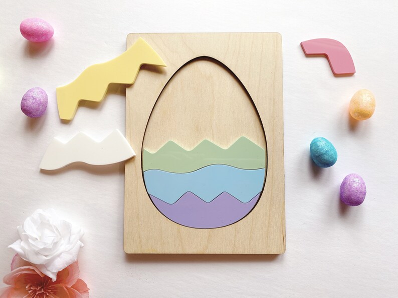 May include: A wooden puzzle board featuring a large egg-shaped cutout. Inside the cutout are three wavy-edged pieces in light green, light blue, and purple. Two additional wavy pieces in yellow and white sit to the left of the board.