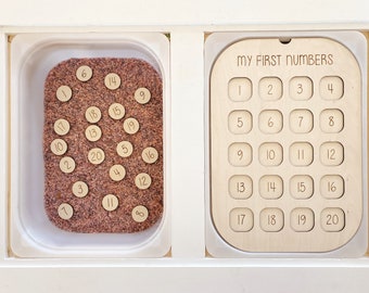 Könnte beinhalten: Ein hölzernes Lernspielzeug mit der Aufschrift "My First Numbers" oben. Das Spielzeug besteht aus zwei Teilen: einer Schale mit 20 nummerierten Holzscheiben und einer Platte mit 20 nummerierten Ausschnitten.