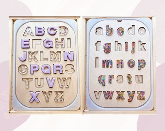 May include: Wooden alphabet puzzle with two trays. One tray has uppercase letters filled with purple glitter. The other tray has lowercase letters filled with colorful sprinkles.