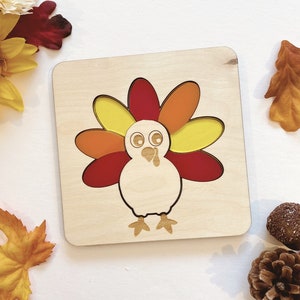 Pu&ograve; includere: Puzzle in legno con un tacchino con piume della coda a motivi rosso, arancione e giallo. Il tacchino ha un corpo bianco e un becco marrone.