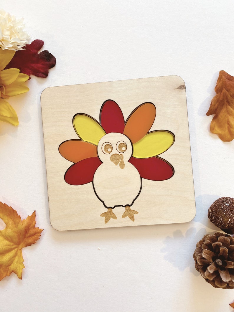 Pu&ograve; includere: Puzzle in legno con un tacchino con piume della coda a motivi rosso, arancione e giallo. Il tacchino ha un corpo bianco e un becco marrone.