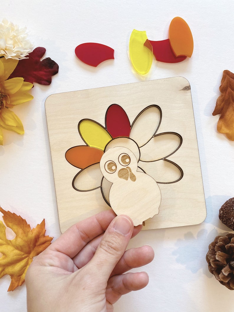 Pu&ograve; includere: Un puzzle di tacchino in legno con pezzi traslucidi colorati. Il tacchino ha un corpo rosso, arancione e giallo e una testa bianca con occhi neri. I pezzi del puzzle sono separati dal tabellone.