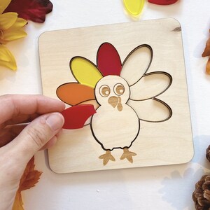 Pu&ograve; includere: Puzzle di legno a forma di tacchino con pezzi traslucidi colorati. Il tacchino ha un corpo rosso, arancione e giallo e una testa bianca con occhi neri. I pezzi hanno la forma di piume e si inseriscono negli incavi corrispondenti sul tabellone.