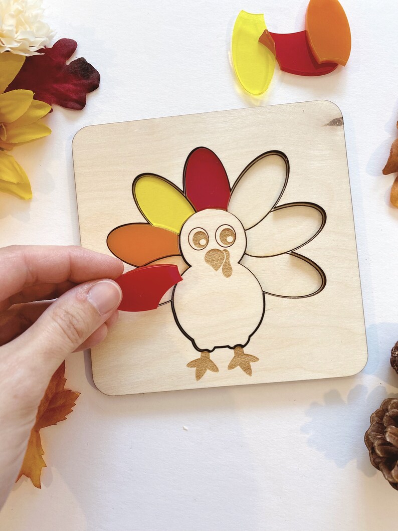 Pu&ograve; includere: Puzzle di legno a forma di tacchino con pezzi traslucidi colorati. Il tacchino ha un corpo rosso, arancione e giallo e una testa bianca con occhi neri. I pezzi hanno la forma di piume e si inseriscono negli incavi corrispondenti sul tabellone.