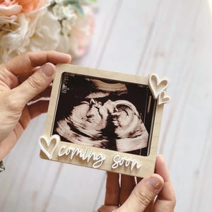 May include: A wooden picture frame with a white heart and the text "coming soon" on the bottom. The frame holds a black and white ultrasound image.