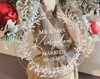 Pode incluir: Ornamento redondo transparente com um design de coroa de flores branca e o texto "MR & MRS Kingdom Married 06.20.2022".