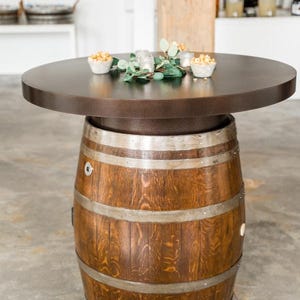May include: A round wooden table with a brown top and a metal base. The base is made of a barrel with metal bands. The table is decorated with greenery and small bowls of popcorn.