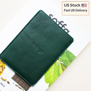 May include: A dark green leather sleeve with the word "voyage" embossed on the front. The sleeve is rectangular with rounded corners. The background includes a magazine with the word "soffa" and a US Stock delivery notice.