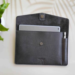 May include: Dark gray leather tablet sleeve with a magnetic snap closure. The sleeve has a textured surface and a pocket for a stylus. The word "voyage" is embossed on the front.