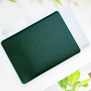 Könnte beinhalten: Eine dunkelgrüne Laptoptasche aus Leder mit dem geprägten Wort "Voyage" auf der Vorderseite.