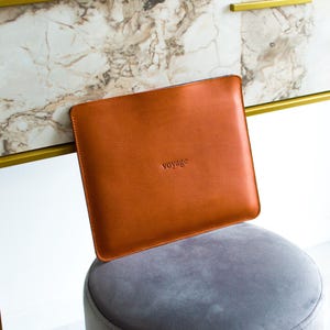 May include: A brown leather laptop sleeve with the word "voyage" embossed on the front.