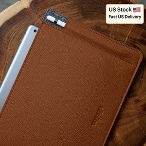 May include: A brown leather tablet sleeve with a matching stylus and a gray felt pocket. The tablet is partially visible, and the sleeve has a textured surface. The text "US Stock Fast US Delivery" is in the upper right corner.