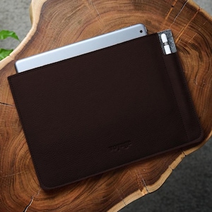 May include: A dark brown leather tablet sleeve with a silver tablet partially inserted. A stylus is in a side pocket. The sleeve is on a wooden surface. The word "voyage" is embossed on the lower right corner.