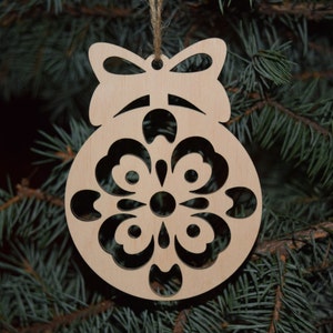 May include: A wooden Christmas ornament shaped like a ball with a snowflake design cut out. The ornament has a bow at the top and is hanging from a string.