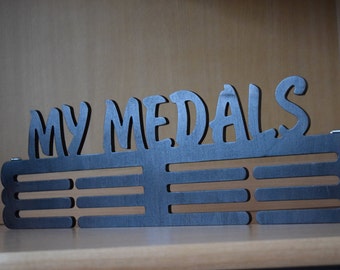 Könnte beinhalten: Schwarzer Medaillenhalter aus Metall mit den ausgeschnittenen Worten "MY MEDALS" oben. Der Halter hat 6 Reihen mit Haken zum Aufhängen von Medaillen.