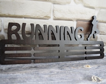 Könnte beinhalten: Ein dunkelbrauner, hölzerner Medaillenhalter mit dem Wort "RUNNING" ausgeschnitten in der Oberseite. Der Halter hat 8 Fächer für Medaillen und eine Silhouette eines Läufers auf der rechten Seite.