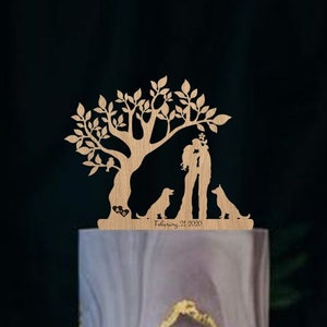 May include: A three-tiered wedding cake with a marble-like gray and gold design. The cake is decorated with white roses and green leaves. A wooden cake topper features a couple kissing under a tree with two dogs and the text "February 21, 2023".