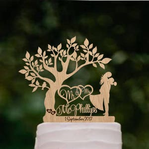 May include: A three-tiered purple ombre wedding cake with a wooden cake topper featuring a tree, two birds, a couple holding hands, and the text "Mr. & Mrs. Phillips 1 September 2017".