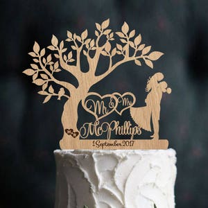 May include: A wooden wedding cake topper featuring a tree with two birds, a couple holding hands, and the text "Mr. & Mrs. Mc Phillips 1 September 2017".