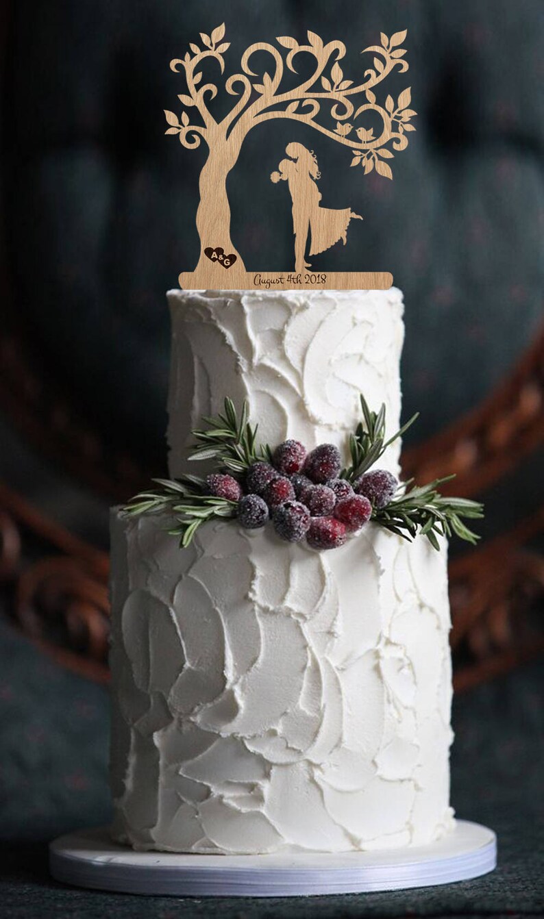 Puede incluir: Un adorno de pastel de boda de madera con una pareja bes&aacute;ndose bajo un &aacute;rbol con p&aacute;jaros posados en las ramas. El adorno est&aacute; personalizado con las iniciales "A & G" y la fecha "August 4th 2018".