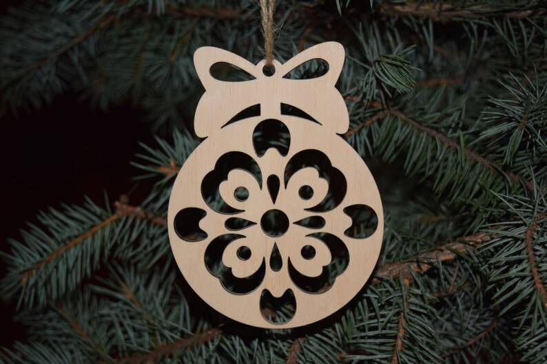 May include: A wooden Christmas ornament shaped like a ball with a snowflake design cut out. The ornament has a bow at the top and is hanging from a string.
