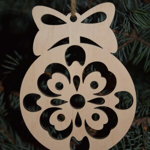 May include: A wooden Christmas ornament shaped like a bell with a bow at the top. The bell has a cut-out design of a flower with intricate details.