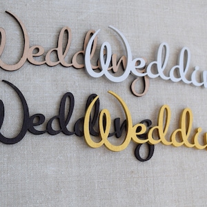 May include: Four wooden "Wedding" signs in different colours: natural wood, white, black, and gold. The signs are all in the same cursive font.
