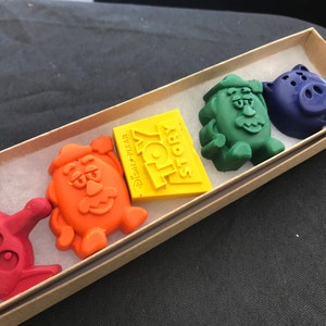 May include: A set of five Toy Story character crayons in a cardboard box. The crayons are shaped like Buzz Lightyear, Woody, Mr. Potato Head, Hamm, and the Toy Story logo. The crayons are red, orange, yellow, green, and purple.