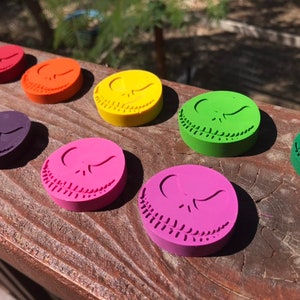 Peut inclure: Un ensemble de neuf crayons ronds, chacun présentant une couleur différente et un motif en relief du visage de Jack Skellington du film L'Étrange Noël de monsieur Jack. Les couleurs sont rouge, orange, jaune, vert, violet, bleu, rose, marron et noir.
