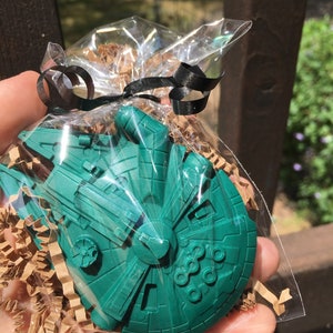 Puede incluir: Un modelo de plástico verde del Millennium Falcon, la nave espacial de Star Wars, envuelto en plástico transparente y atado con una cinta negra.