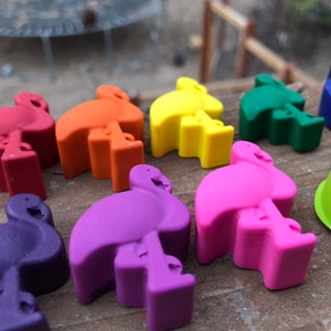 May include: A selection of brightly coloured flamingo-shaped erasers. The erasers are in shades of red, orange, yellow, green, blue, purple, and pink. They are arranged on a wooden surface, highlighting their vibrant colours and playful design.