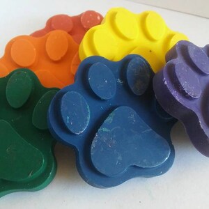 May include: Five colorful paw print shaped crayons in green, blue, orange, yellow, and purple.