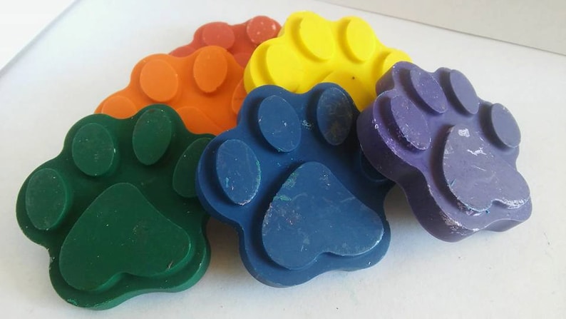 May include: Five colorful paw print shaped crayons in green, blue, orange, yellow, and purple.