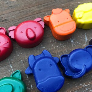 Puede incluir: Una colecci&oacute;n de ceras de colores con forma de animales en rojo, naranja, amarillo, verde, azul y morado. Las ceras est&aacute;n dispuestas sobre una superficie de madera envejecida. Las formas de animales incluyen un gato, un koala, una vaca y un elefante.