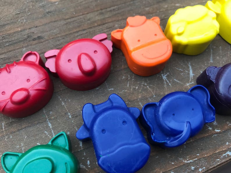 Puede incluir: Una colecci&oacute;n de ceras de colores con forma de animales en rojo, naranja, amarillo, verde, azul y morado. Las ceras est&aacute;n dispuestas sobre una superficie de madera envejecida. Las formas de animales incluyen un gato, un koala, una vaca y un elefante.