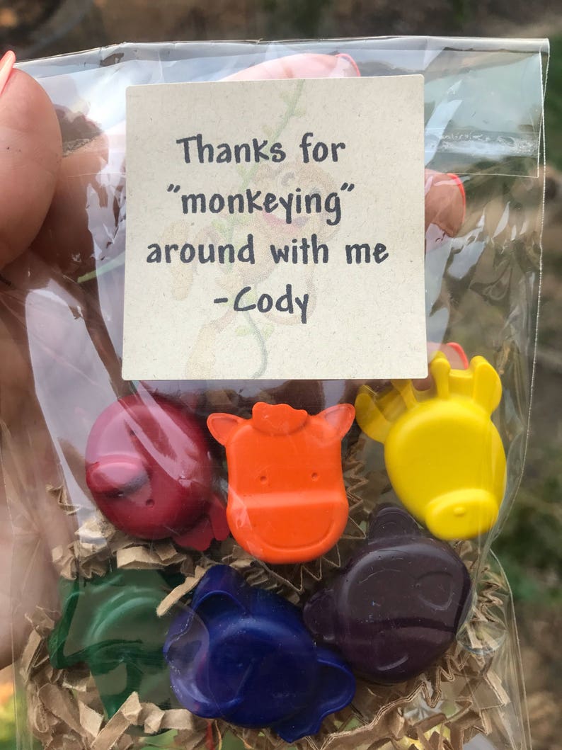 Puede incluir: Una bolsa transparente llena de crayones con forma de animales de varios colores. Los crayones son rojos, naranjas, amarillos, verdes, azules y morados. Una peque&ntilde;a tarjeta dice: "Gracias por 'monear' conmigo - Cody."