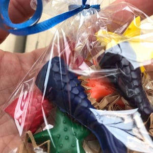 Könnte beinhalten: Eine durchsichtige Plastiktüte gefüllt mit bunten Wachsmalstiften in Form einer Meerjungfrauenflosse, eines Seesterns und eines Fisches. Die Tüte ist mit einem blauen Band gebunden.