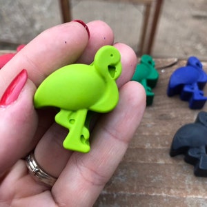 May include: A selection of flamingo-shaped bottle stoppers in various colours. The stoppers are in green, red, blue, and black. The flamingo stoppers are made of a solid material and are designed to fit into the top of a bottle.