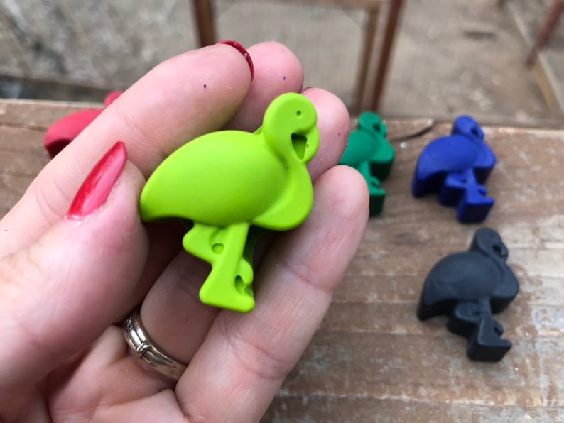 May include: A selection of flamingo-shaped bottle stoppers in various colours. The stoppers are in green, red, blue, and black. The flamingo stoppers are made of a solid material and are designed to fit into the top of a bottle.