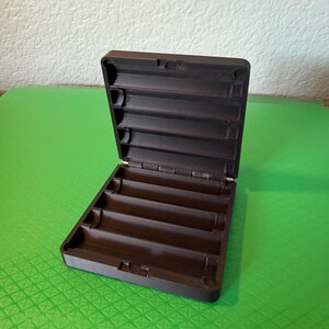 May include: A dark brown, rectangular, hinged storage case featuring a series of horizontal, semi-cylindrical grooves molded into both the interior base and the interior lid. The case is open, revealing a structured, multi-slot interior design.