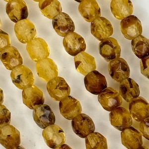 May include: A strand of faceted, golden brown beads. The beads are oval shaped and have a translucent appearance.