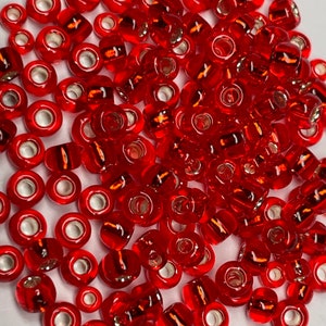 May include: A large pile of red glass seed beads with silver-toned metal caps. The beads are round and have a shiny finish.