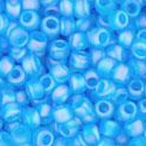 May include: A close-up shot of a pile of small, light blue seed beads. The beads are cylindrical with a hole running through the center. The beads have a slightly translucent quality, with a hint of white or lighter blue within.