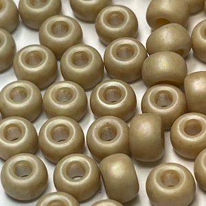 May include: A collection of round, beige seed beads with a slight iridescent sheen. The beads have a hole in the center for stringing.