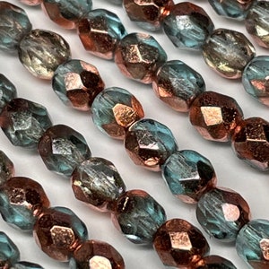 May include: A strand of faceted glass beads with a copper iridescent finish. The beads are a mix of teal and copper colors.
